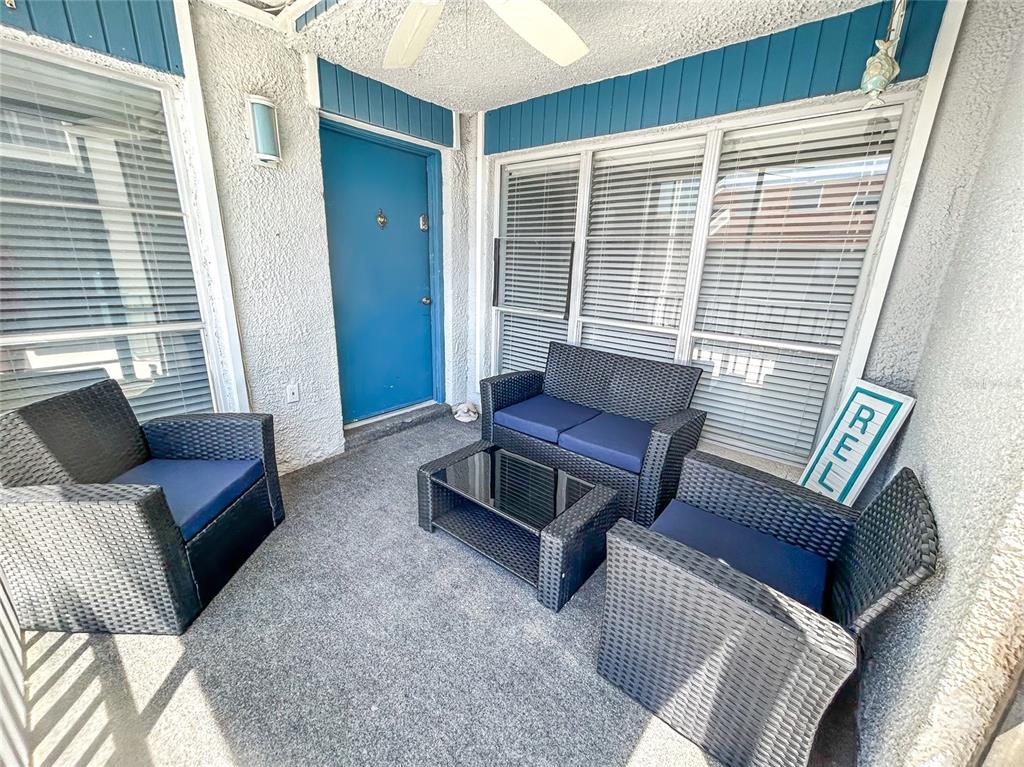 A covered patio features wicker furniture with blue cushions and a blue entry door — 315 MEDALLION BOULEVARD UNIT F, MADEIRA BEACH, FL