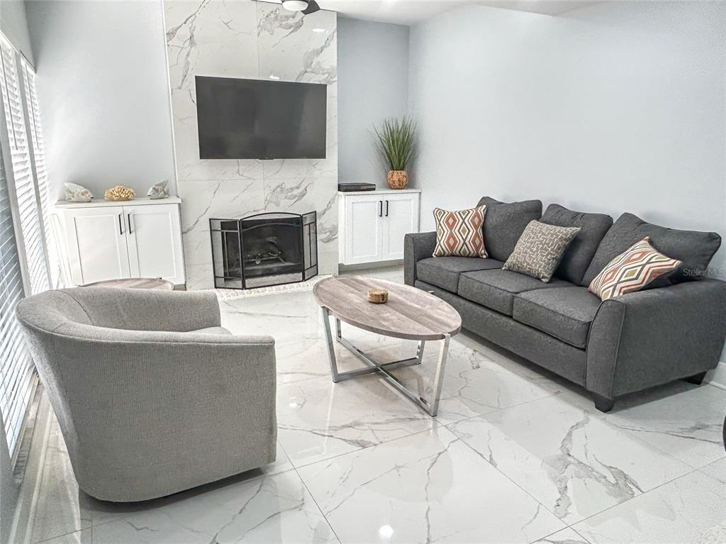 A living room features a marble fireplace, gray sofa, accent chair, and white tile flooring — 315 MEDALLION BOULEVARD UNIT F, MADEIRA BEACH, FL