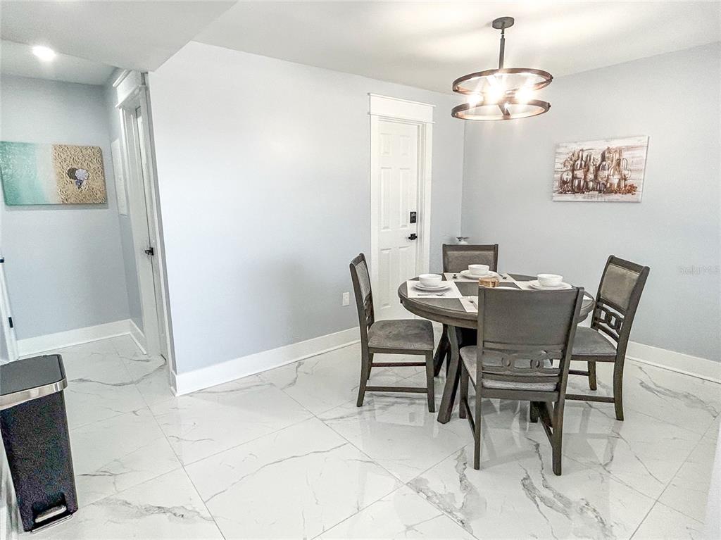 A dining area features a round table with four chairs, a chandelier, and marble-look flooring — 315 MEDALLION BOULEVARD UNIT F, MADEIRA BEACH, FL