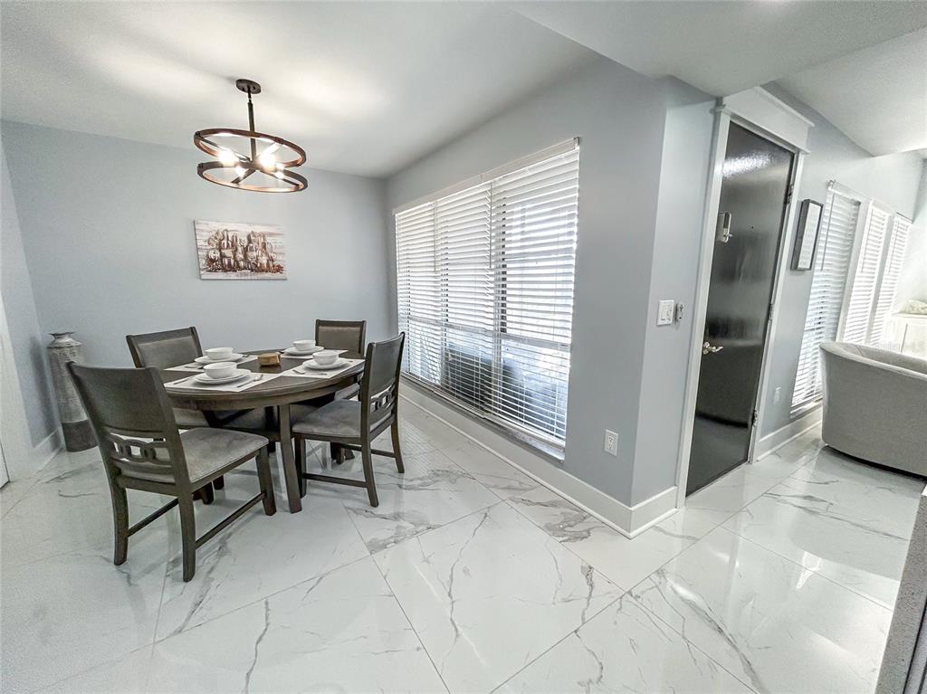 A dining room features a round table, four chairs, a chandelier, and white marble flooring — 315 MEDALLION BOULEVARD UNIT F, MADEIRA BEACH, FL