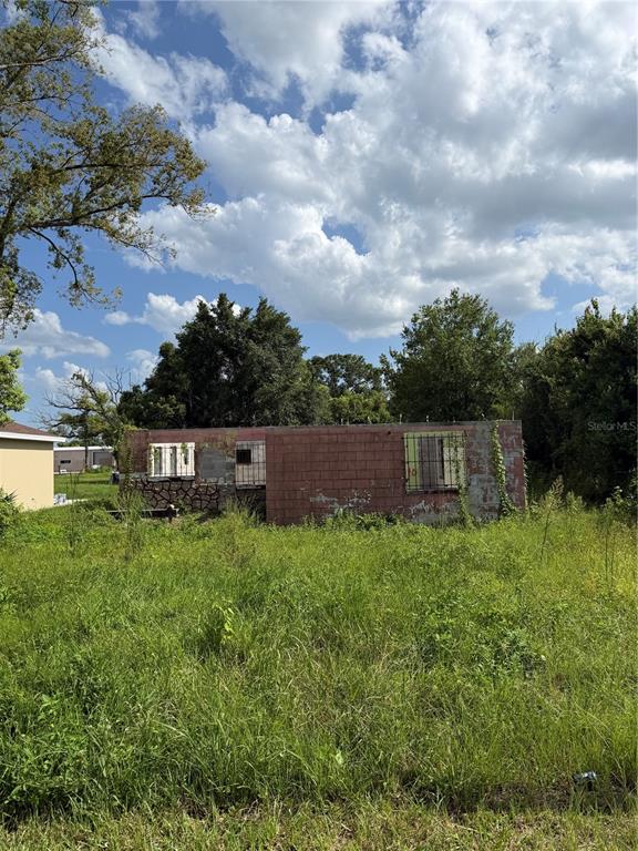 A weathered, single-story concrete block structure sits in a field of tall, overgrown grass — 2661 W 22ND STREET, SANFORD, FL