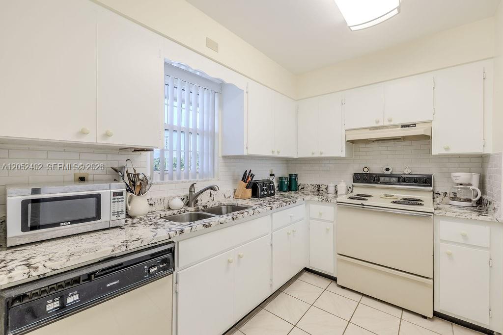 A kitchen features white cabinets, granite countertops, a white stove, and a stainless steel microwave — 2333 Indian River Blvd # 306, Vero Beach FL 32960, VERO BEACH, FL