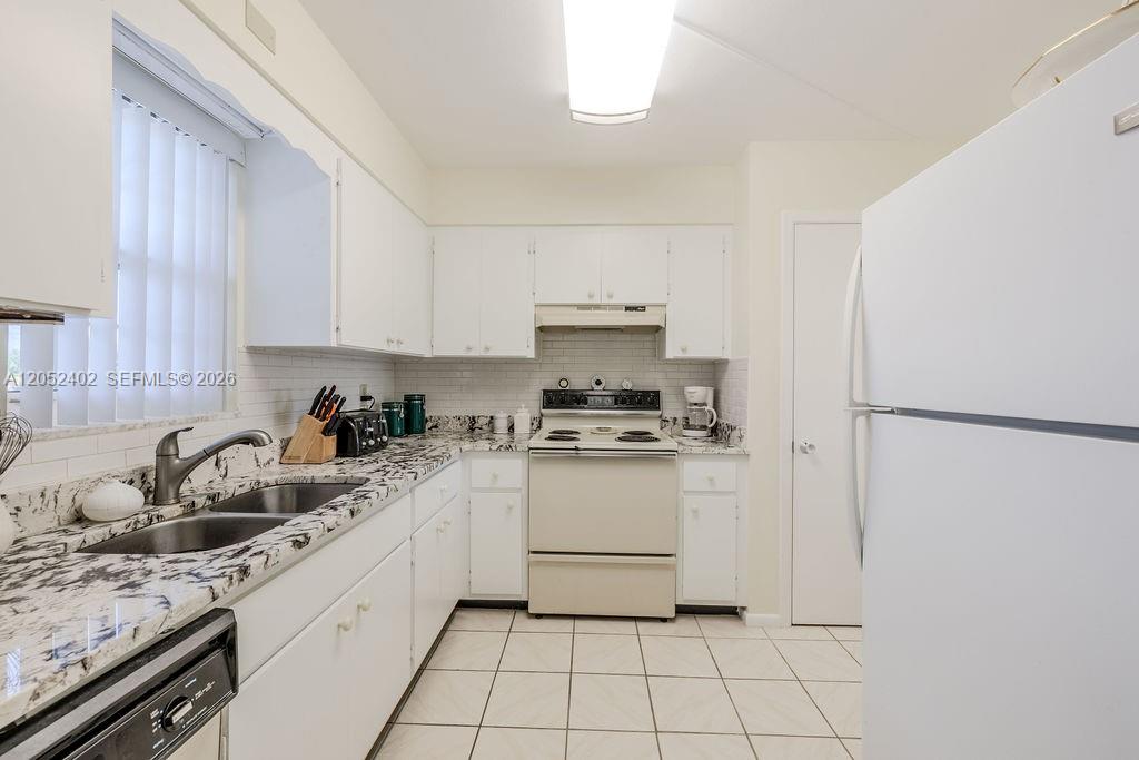 A kitchen features white cabinets, granite countertops, a white stove, and a white refrigerator — 2333 Indian River Blvd # 306, Vero Beach FL 32960, VERO BEACH, FL