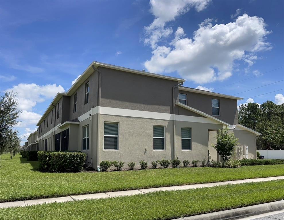 A two-story townhouse exterior with tan and gray stucco walls and a grassy lawn — 15246 HARRINGTON COVE DRIVE, ORLANDO, FL