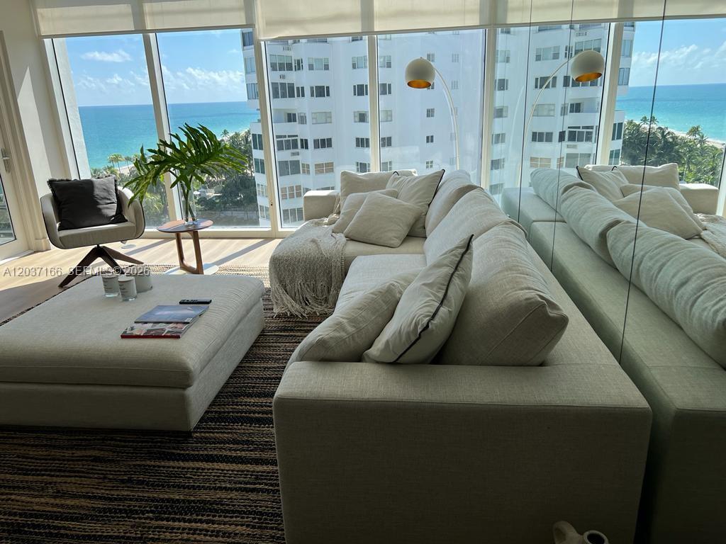 A living room features a light-colored sectional sofa, ottoman, and floor-to-ceiling windows overlooking the ocean — 10275 Collins Ave # 915, Bal Harbour FL 33154, BAL HARBOUR, FL