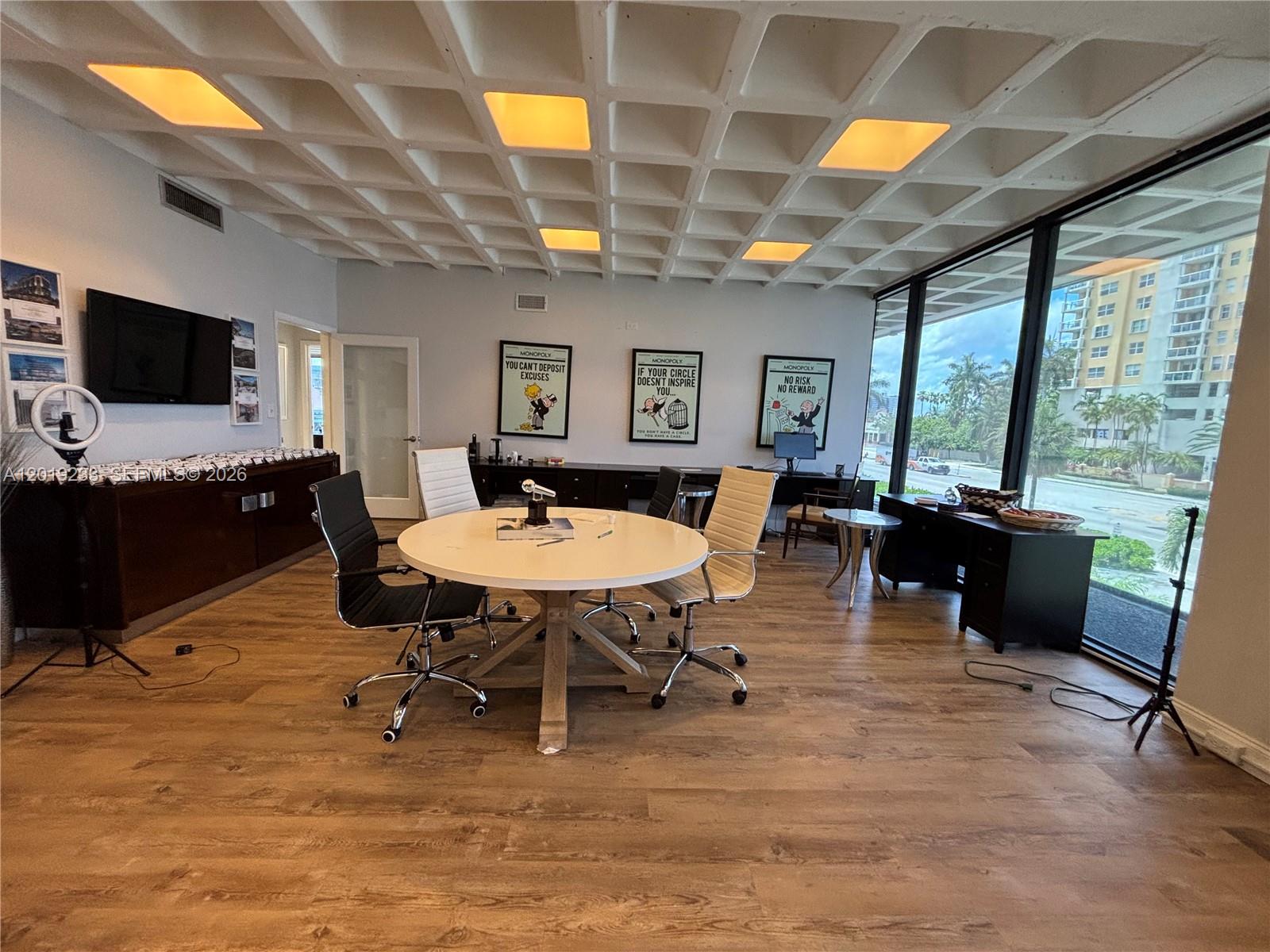 An office features a round table, chairs, a coffered ceiling, and large windows overlooking buildings — NORTH BAY VILLAGE, FL