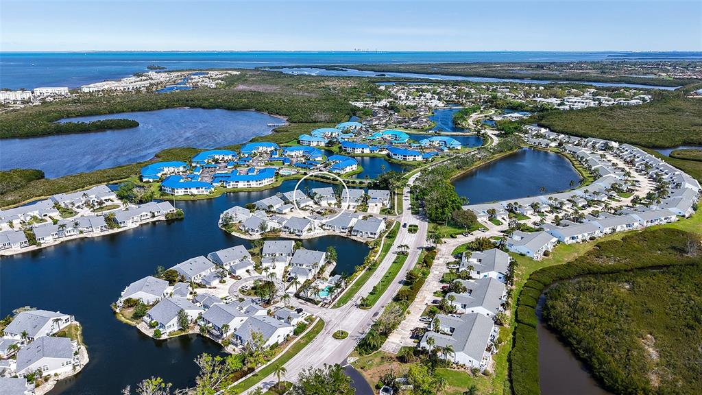 An aerial view shows a residential community with blue-roofed buildings surrounded by water and mangroves — 1005 PELICAN COURT, BRADENTON, FL