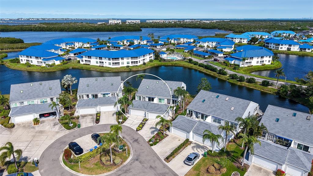 An aerial view shows a residential complex with blue-roofed buildings surrounding a central pond — 1005 PELICAN COURT, BRADENTON, FL