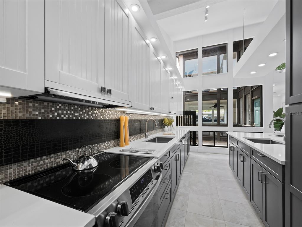 A modern galley kitchen features white upper cabinets, dark lower cabinets, and a tiled backsplash — 800 S BLVD OF THE PRESIDENTS UNIT 19, SARASOTA, FL