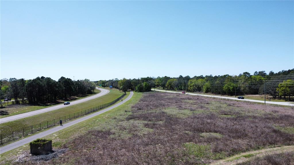 An aerial view shows a paved trail running alongside a highway next to a vacant field — 1290 ANDERSON SNOW ROAD, SPRING HILL, FL