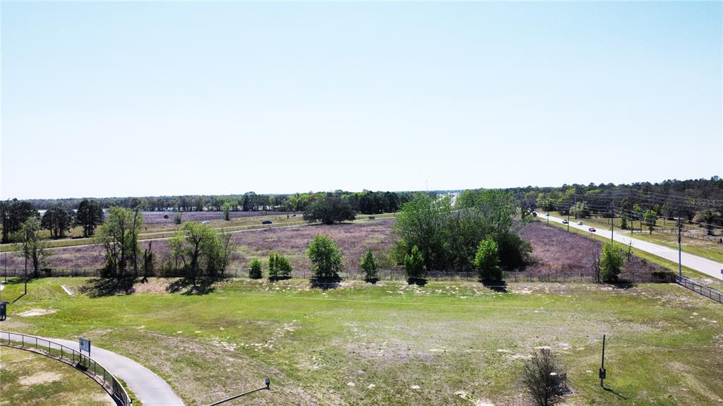 An aerial view shows a large, grassy field adjacent to an undeveloped, brush-covered lot — 1290 ANDERSON SNOW ROAD, SPRING HILL, FL