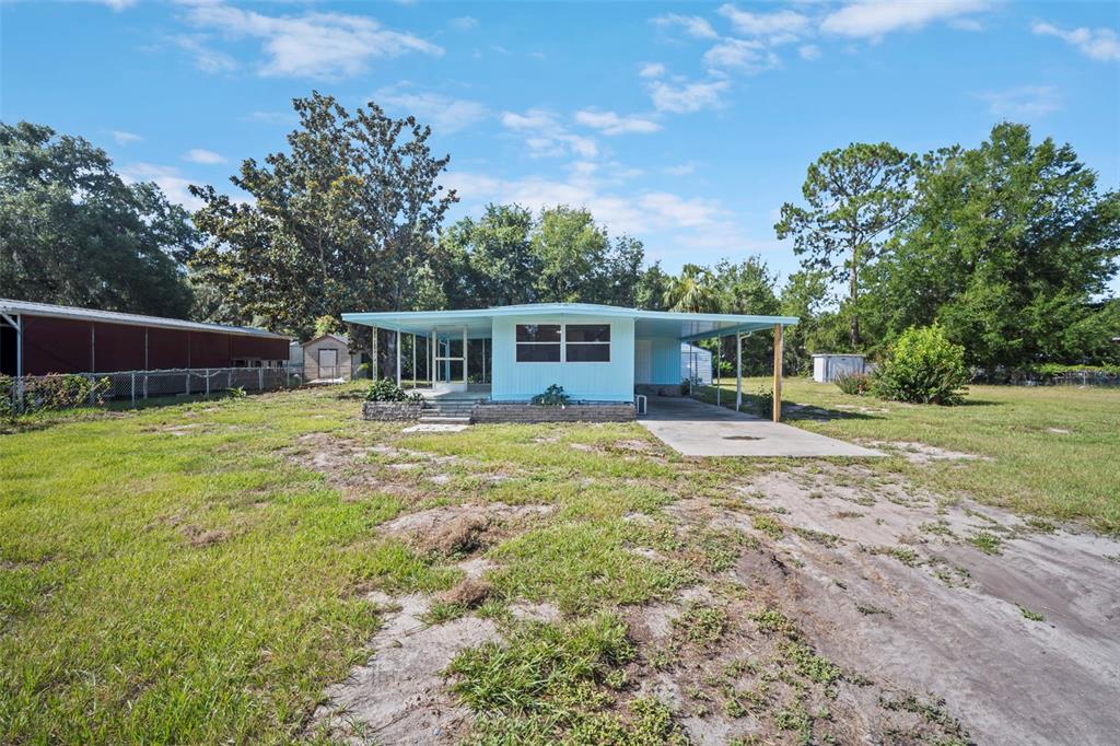A light blue single-story house with a carport and a large grassy yard — 1389 NW 7TH LANE, LAKE PANASOFFKEE, FL
