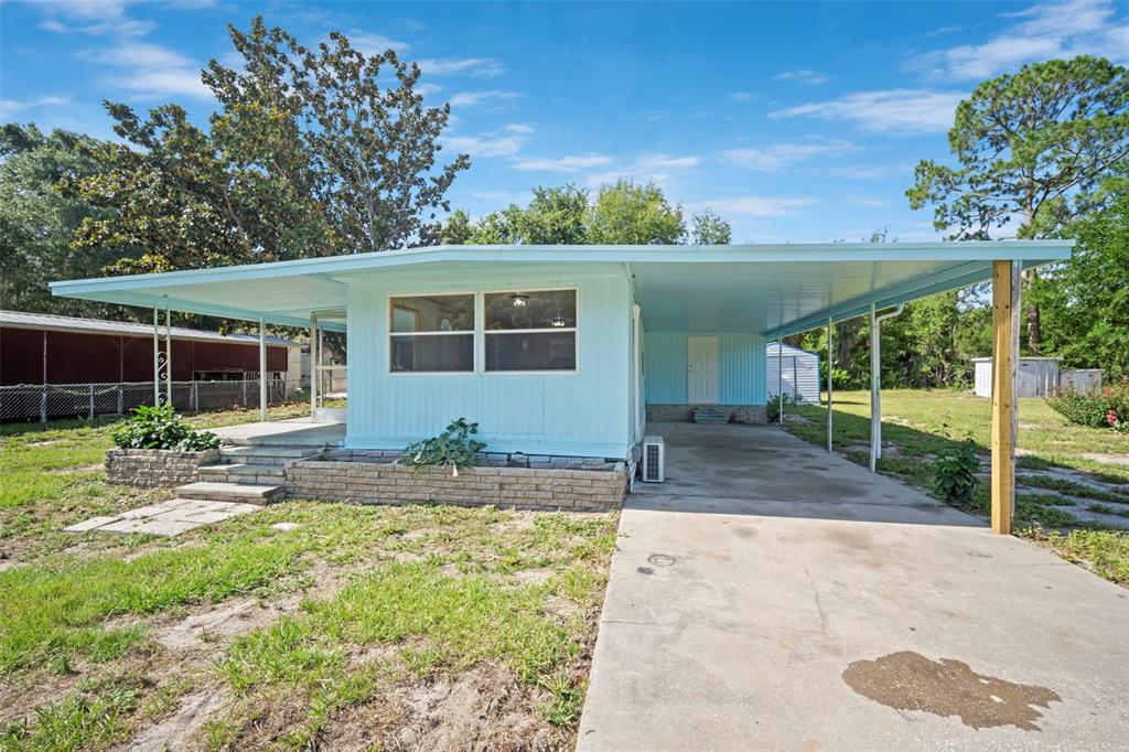 A light blue mobile home features a concrete driveway, a carport, and a brick planter — 1389 NW 7TH LANE, LAKE PANASOFFKEE, FL