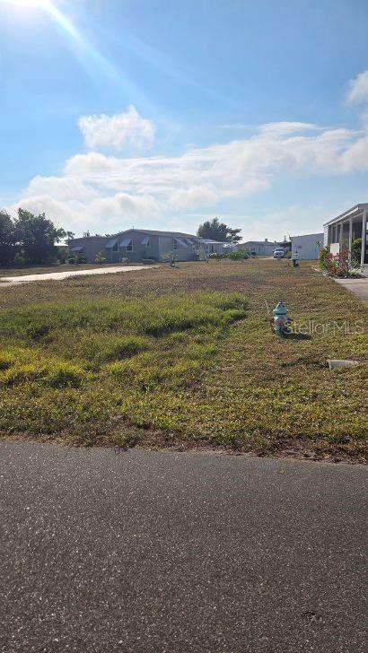 A vacant, grassy lot sits between manufactured homes under a bright blue sky — 1365 SANDERLING DRIVE, ENGLEWOOD, FL