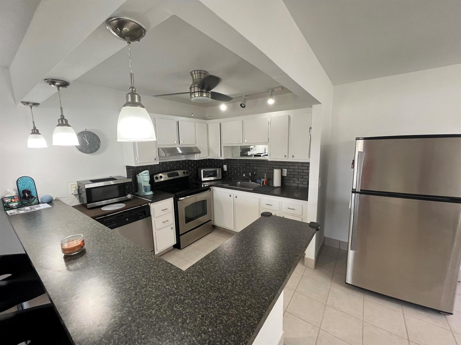 A kitchen features white cabinets, dark countertops, stainless steel appliances, and a breakfast bar — 114 Waterford E # 114, Delray Beach FL 33446, DELRAY BEACH, FL