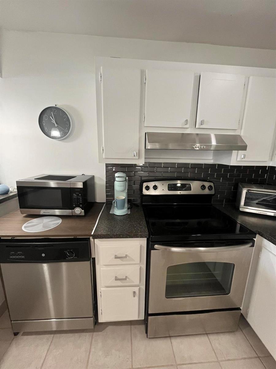 A kitchen features white cabinets, stainless steel appliances, and a dark subway tile backsplash — 114 Waterford E # 114, Delray Beach FL 33446, DELRAY BEACH, FL