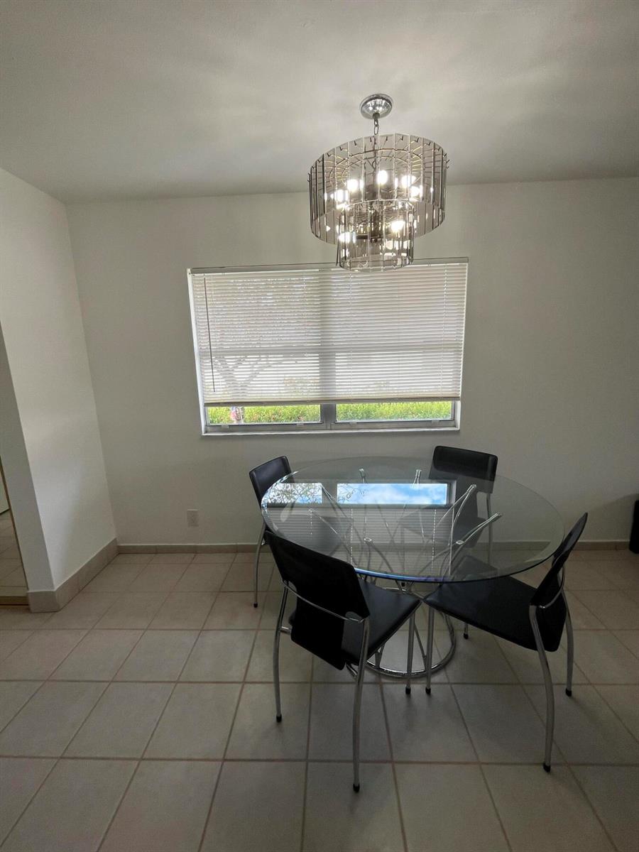 A dining area with a glass table, four black chairs, and a modern crystal chandelier — 114 Waterford E # 114, Delray Beach FL 33446, DELRAY BEACH, FL