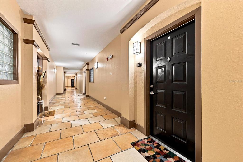 A hallway with tan tile flooring leads past a black door toward a distant exit — 4221 W SPRUCE STREET UNIT 1419, TAMPA, FL