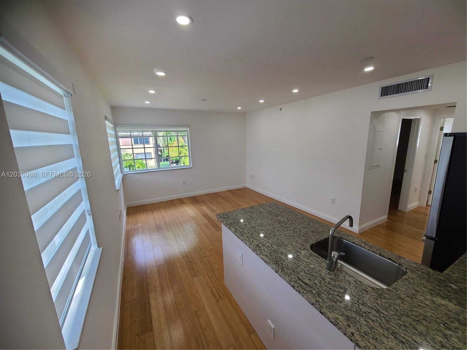 A kitchen island with a granite countertop and sink overlooks an empty living area — 825 Michigan Ave # 3, Miami Beach FL 33139, MIAMI BEACH, FL