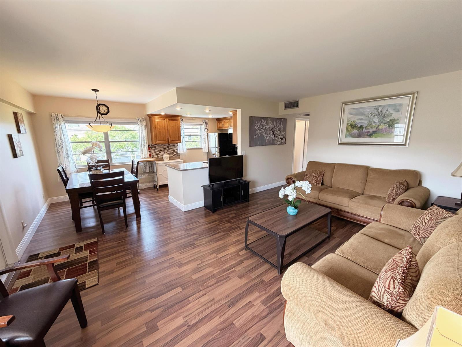 An open-concept living and dining area features wood-look flooring, tan sofas, and a kitchen — 375 Mansfield I, Boca Raton FL 33434, BOCA RATON, FL
