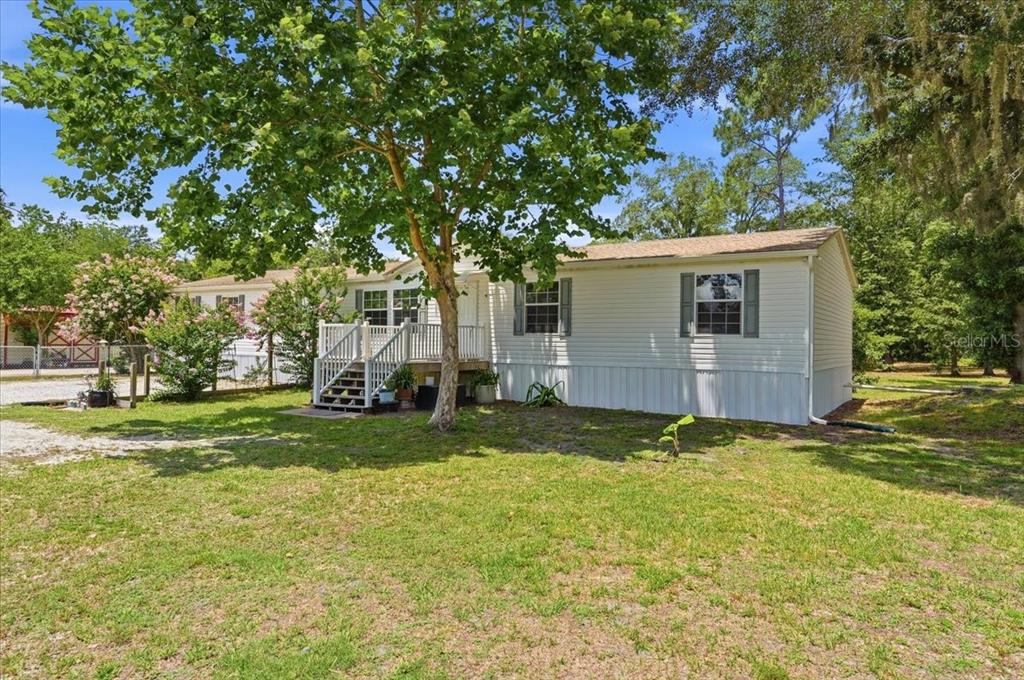 A single-story manufactured home with white siding, a front porch, and a large shade tree — 10626 PATHFINDER TRAIL, LAKELAND, FL