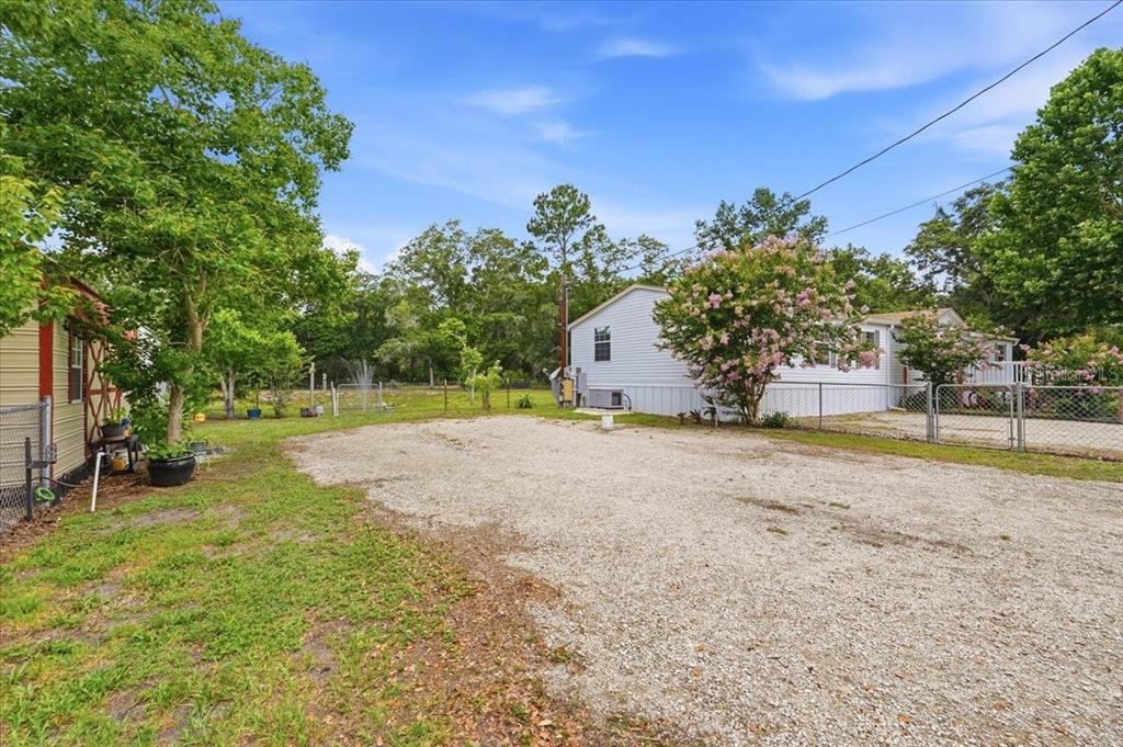 A gravel driveway leads to a white mobile home with a fenced yard and trees — 10626 PATHFINDER TRAIL, LAKELAND, FL