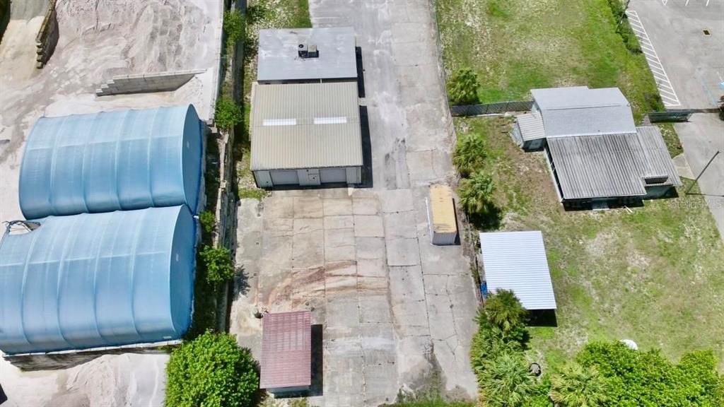 An aerial view shows a commercial property with two large blue structures and a warehouse — 9213 DENTON AVENUE, HUDSON, FL
