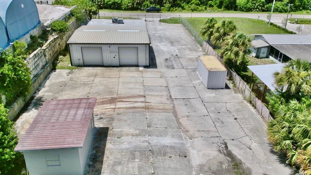 An aerial view shows a commercial property with a warehouse, shed, and concrete parking lot — 9213 DENTON AVENUE, HUDSON, FL