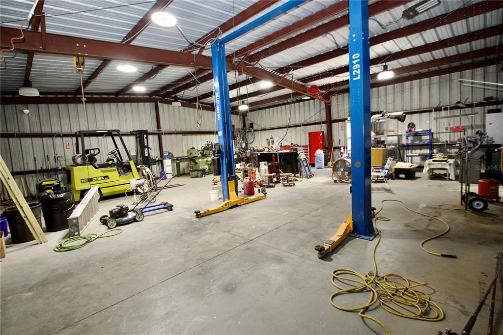 A spacious industrial workshop features a concrete floor, metal walls, and a two-post vehicle lift — 9213 DENTON AVENUE, HUDSON, FL