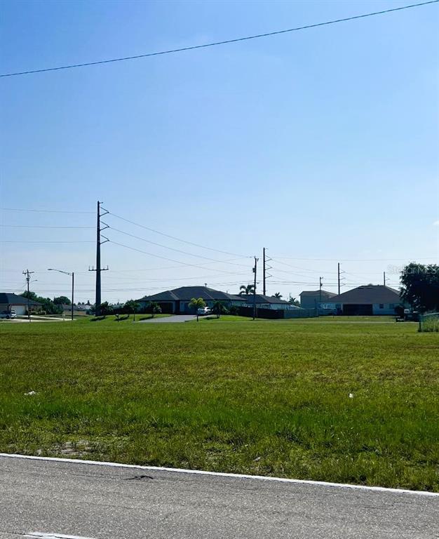 A large, grassy vacant lot sits in front of several suburban houses under a clear sky — 2713 SANTA BARBARA BOULEVARD N, CAPE CORAL, FL