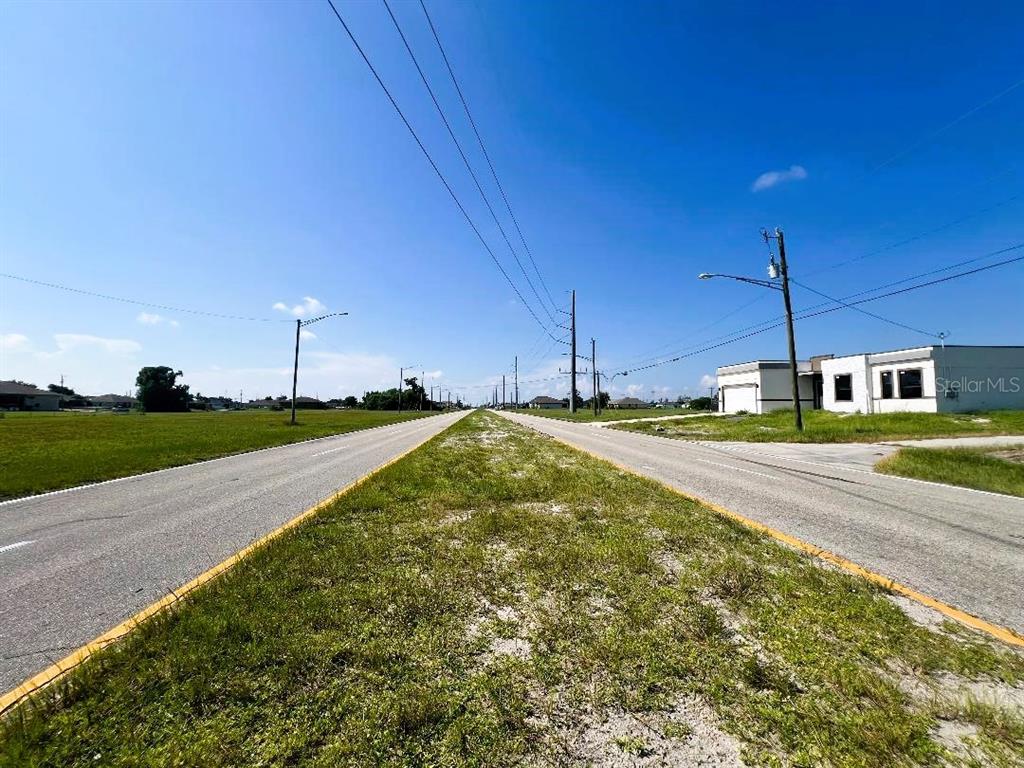 A paved road stretches into the distance between grassy fields under a clear blue sky — 2713 SANTA BARBARA BOULEVARD N, CAPE CORAL, FL