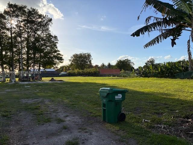 A green trash bin sits on a grassy lot with trees under a blue sky — UNINCORPORATED, Miami FL 33187, MIAMI, FL