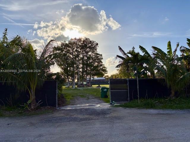 A gated gravel driveway leads to a grassy area with trees under a sunny sky — UNINCORPORATED, Miami FL 33187, MIAMI, FL