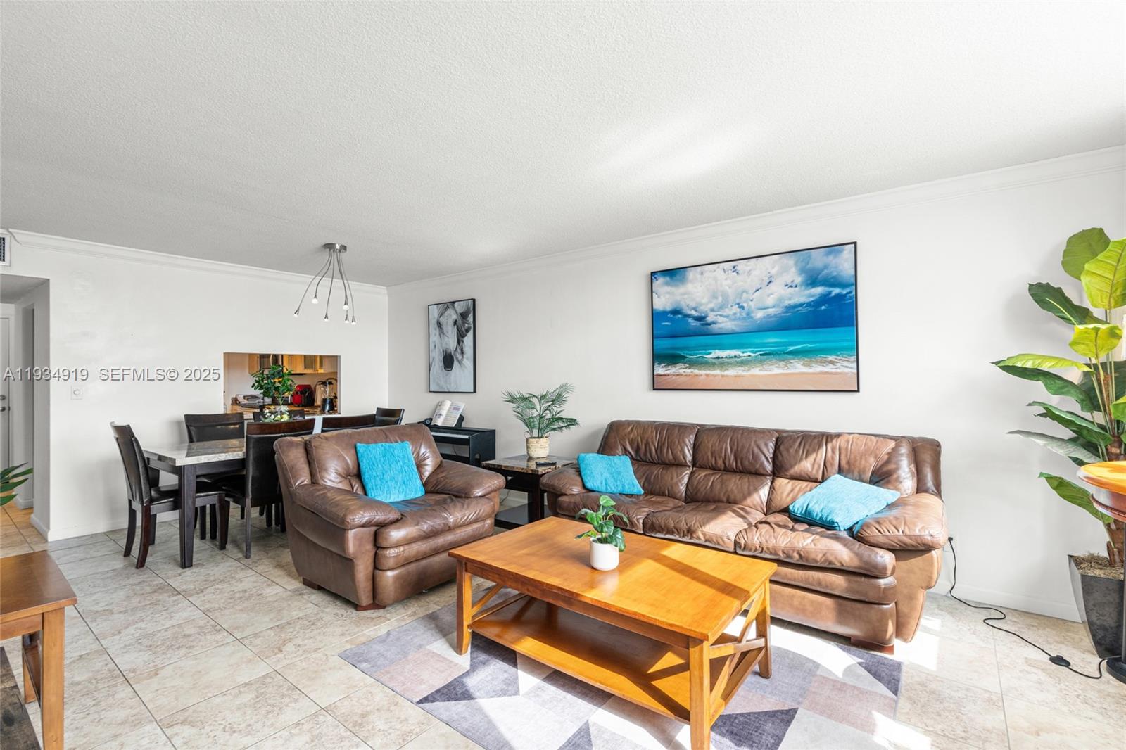 A living room with tile flooring, brown leather furniture, and a large beach wall art — 1170 NE 191st St # 35, Miami FL 33179, MIAMI, FL
