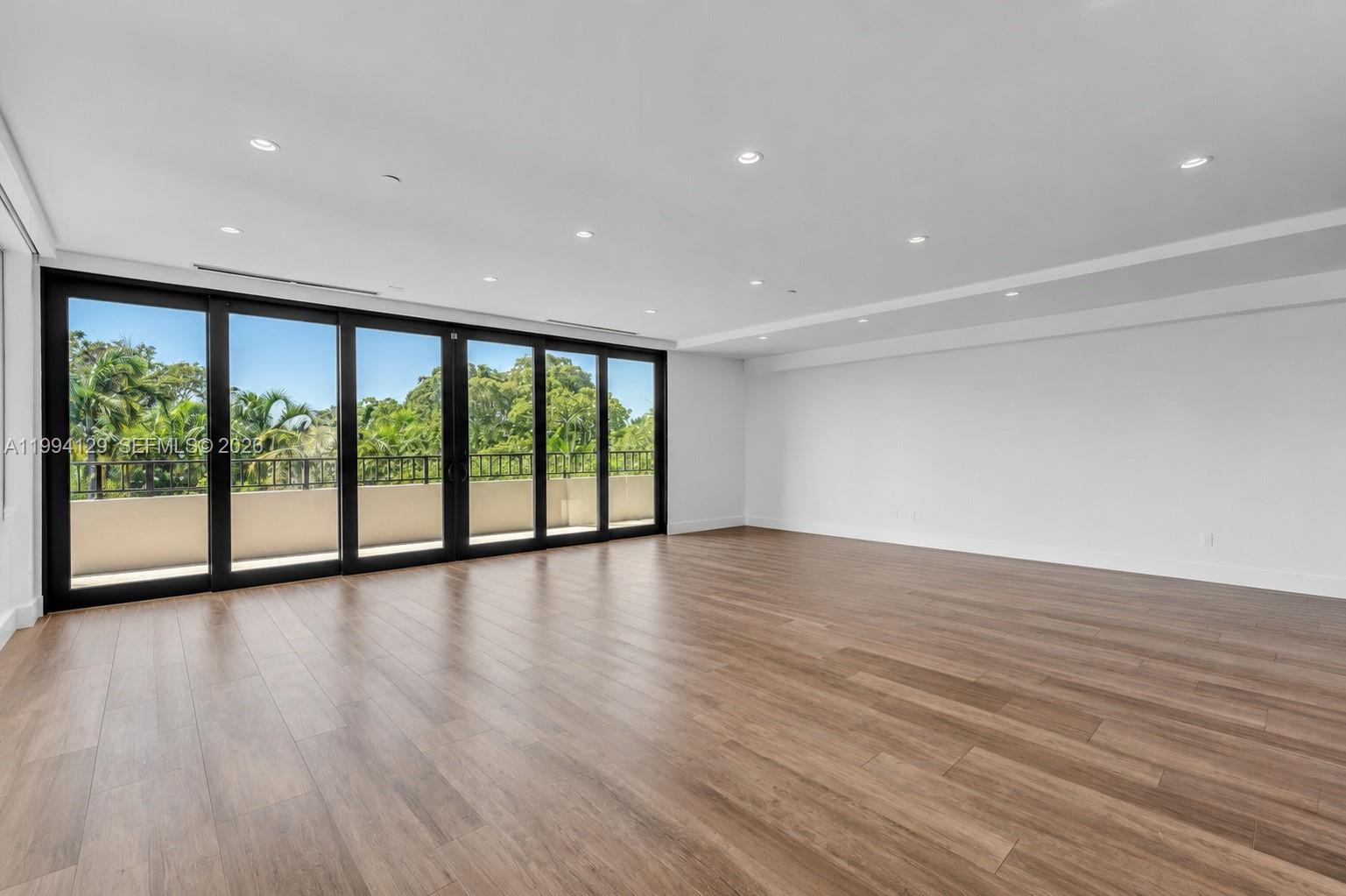 An empty room features wood-look flooring, white walls, recessed lighting, and large sliding glass doors — 151 Crandon Blvd # 345, Key Biscayne FL 33149, KEY BISCAYNE, FL