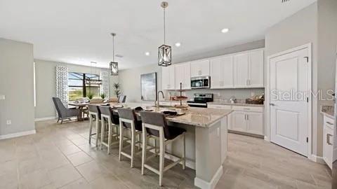 A modern kitchen features white cabinetry, a large island with bar seating, and tile flooring — 3280 ALTIMIRA DRIVE, FORT MYERS, FL