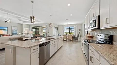 A modern kitchen features white cabinetry, granite countertops, a large island, and stainless steel appliances — 3280 ALTIMIRA DRIVE, FORT MYERS, FL