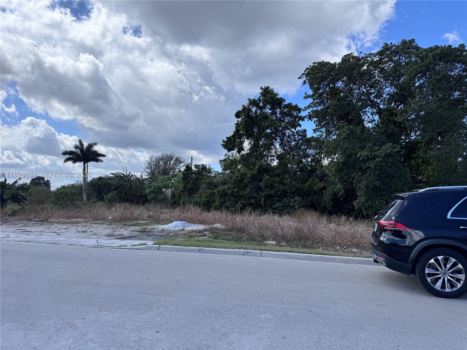A black SUV is parked on a paved road next to a vacant, overgrown grassy lot — 875 JOE LOUIS AVE, Pahokee FL 33476, PAHOKEE, FL