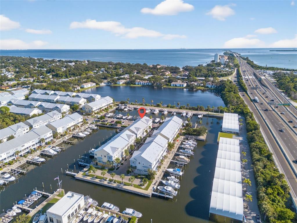 An aerial view shows a waterfront residential complex with boat slips and a nearby highway — 6080 MOORINGS DRIVE S, ST PETERSBURG, FL