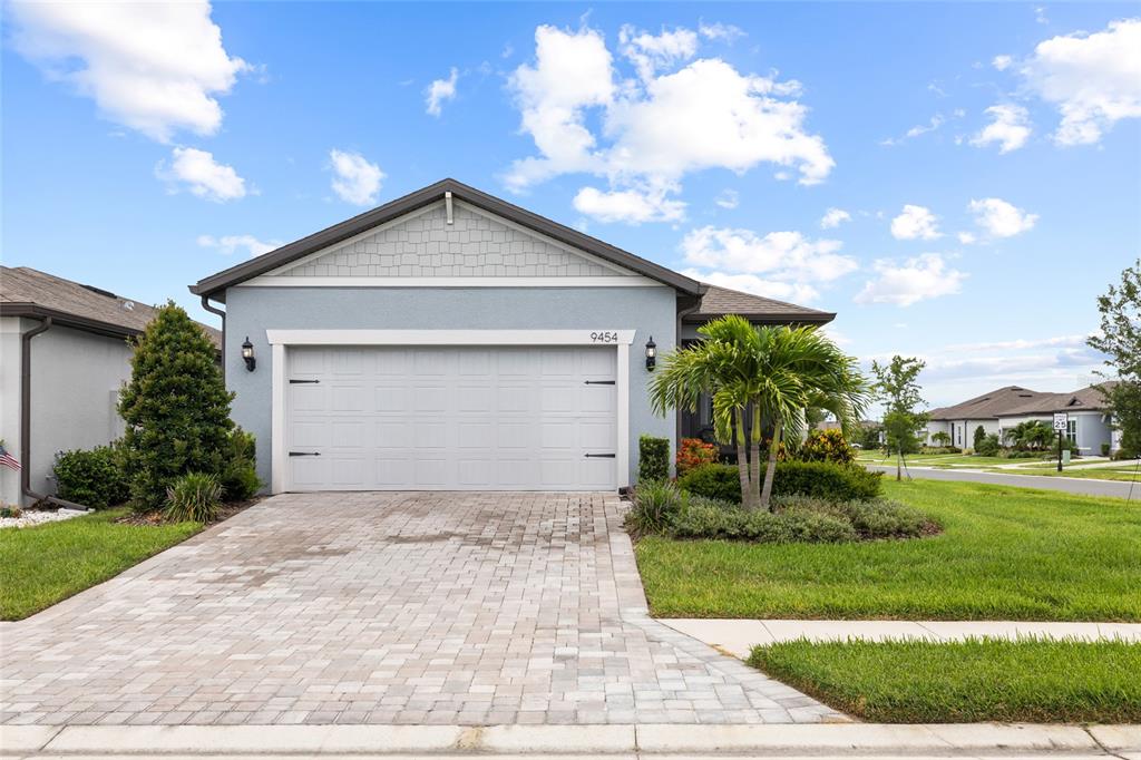 A light blue house features a two-car garage, a paver driveway, and a palm tree — 9454 BALLASTER POINTE LOOP, PARRISH, FL