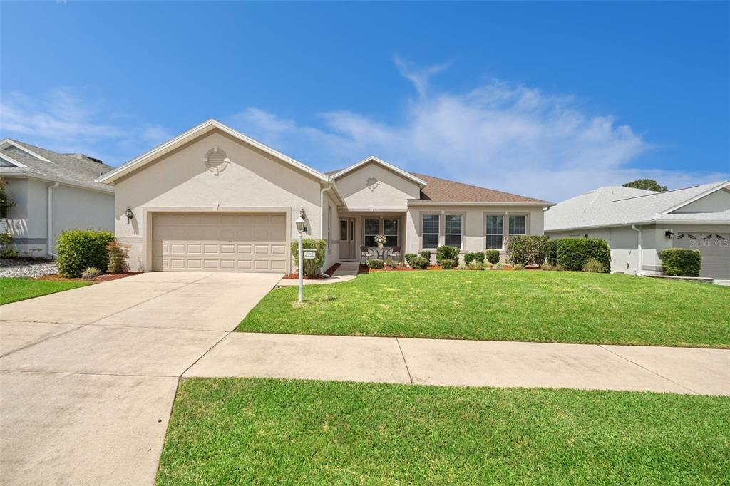 A single-story suburban house with a beige stucco exterior, a two-car garage, and a lawn — 3719 BELLE ROSE DRIVE, LEESBURG, FL