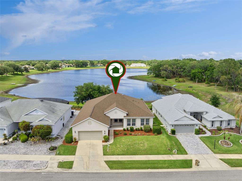 An aerial view shows a single-story house with a brown roof facing a lake — 3719 BELLE ROSE DRIVE, LEESBURG, FL