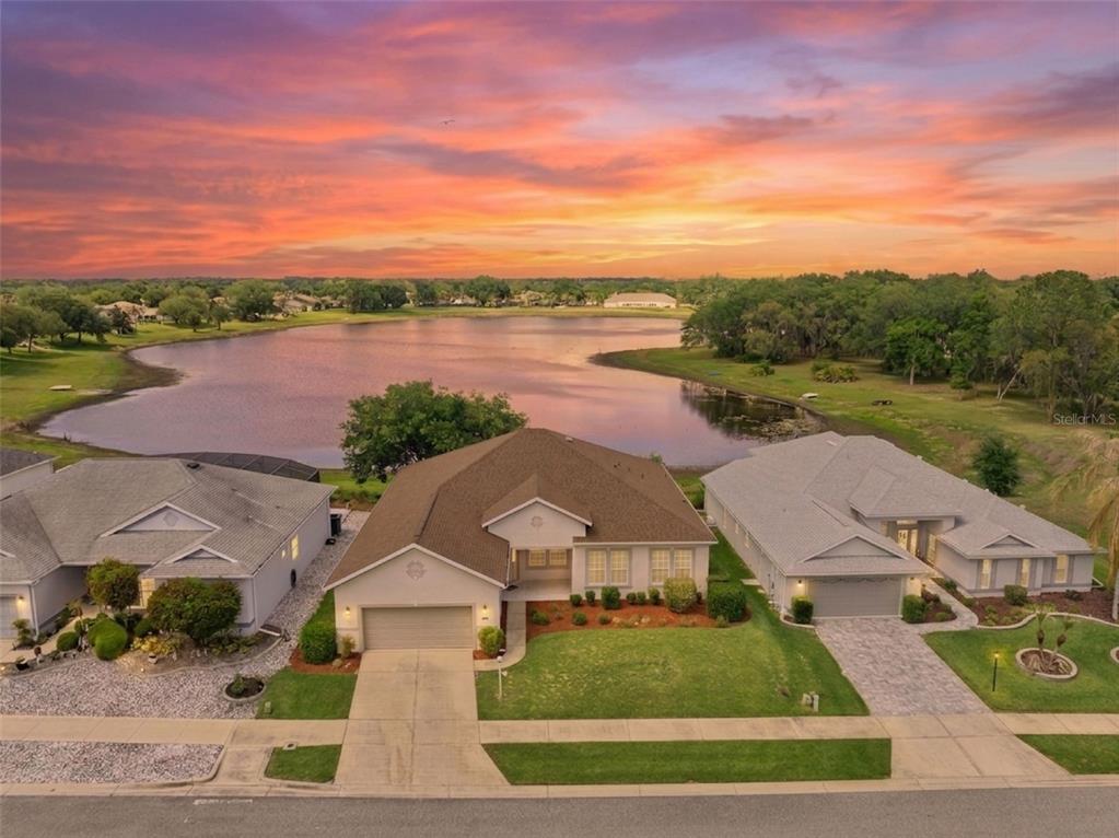 An aerial view shows a suburban house with a lake in the background at sunset — 3719 BELLE ROSE DRIVE, LEESBURG, FL