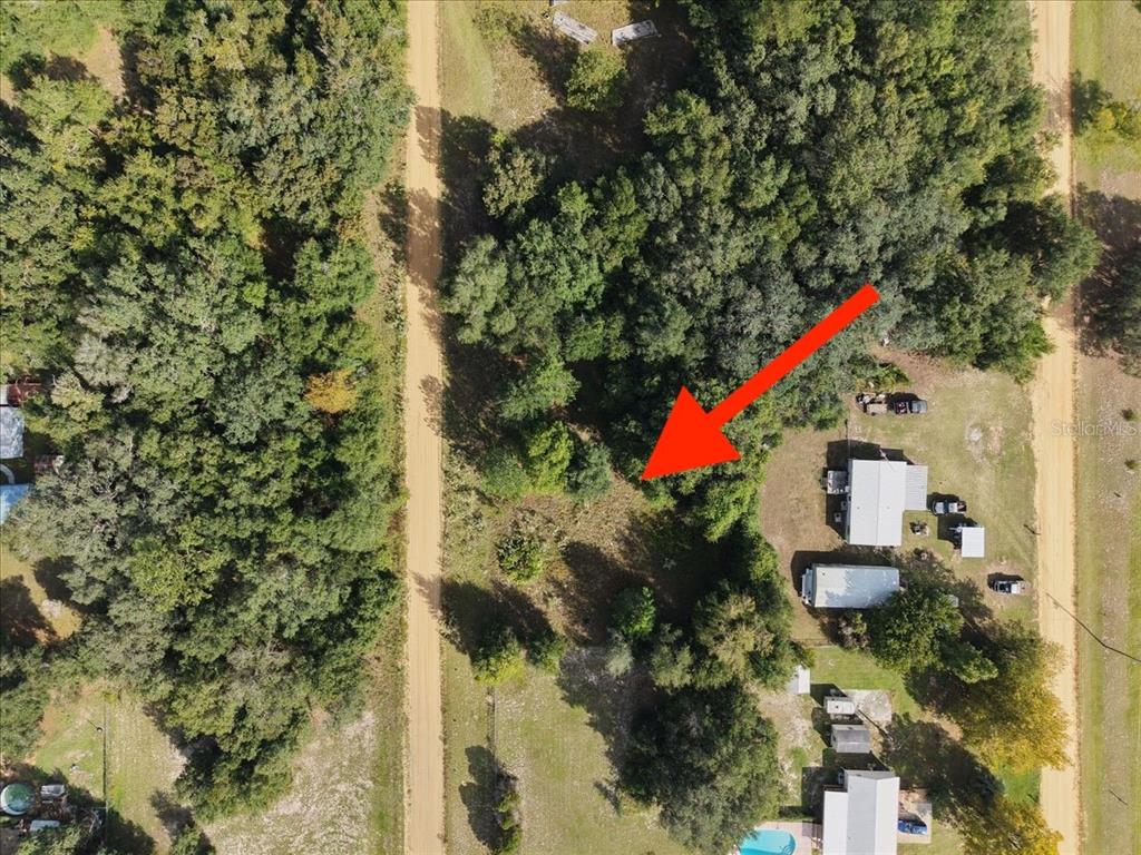 An aerial view shows a wooded lot situated between two dirt roads — 208 N HELMERS AVENUE, INTERLACHEN, FL