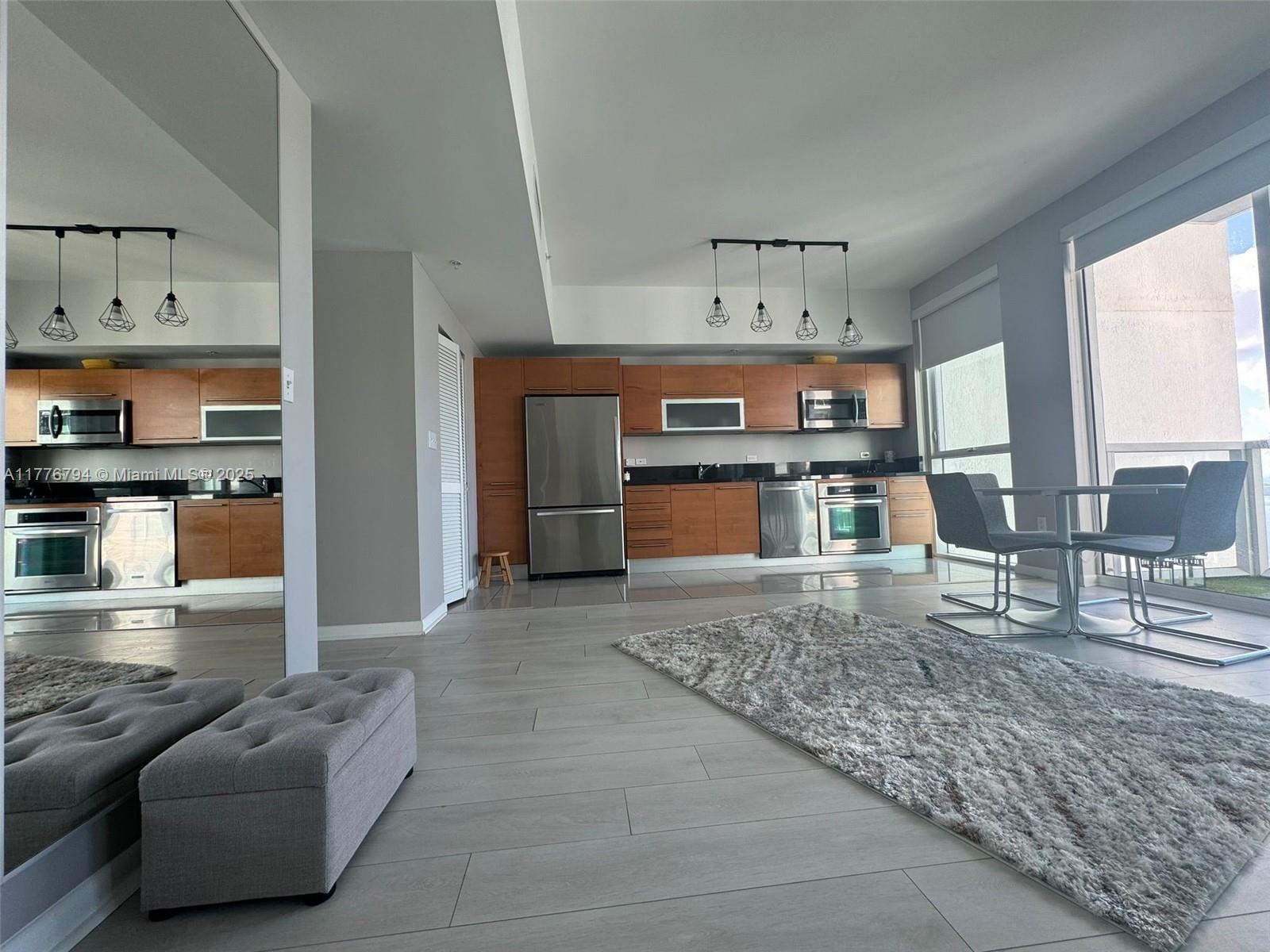 A modern kitchen with wood cabinets and stainless steel appliances opens to a dining area — 244 Biscayne Blvd # 3905, Miami FL 33132, MIAMI, FL
