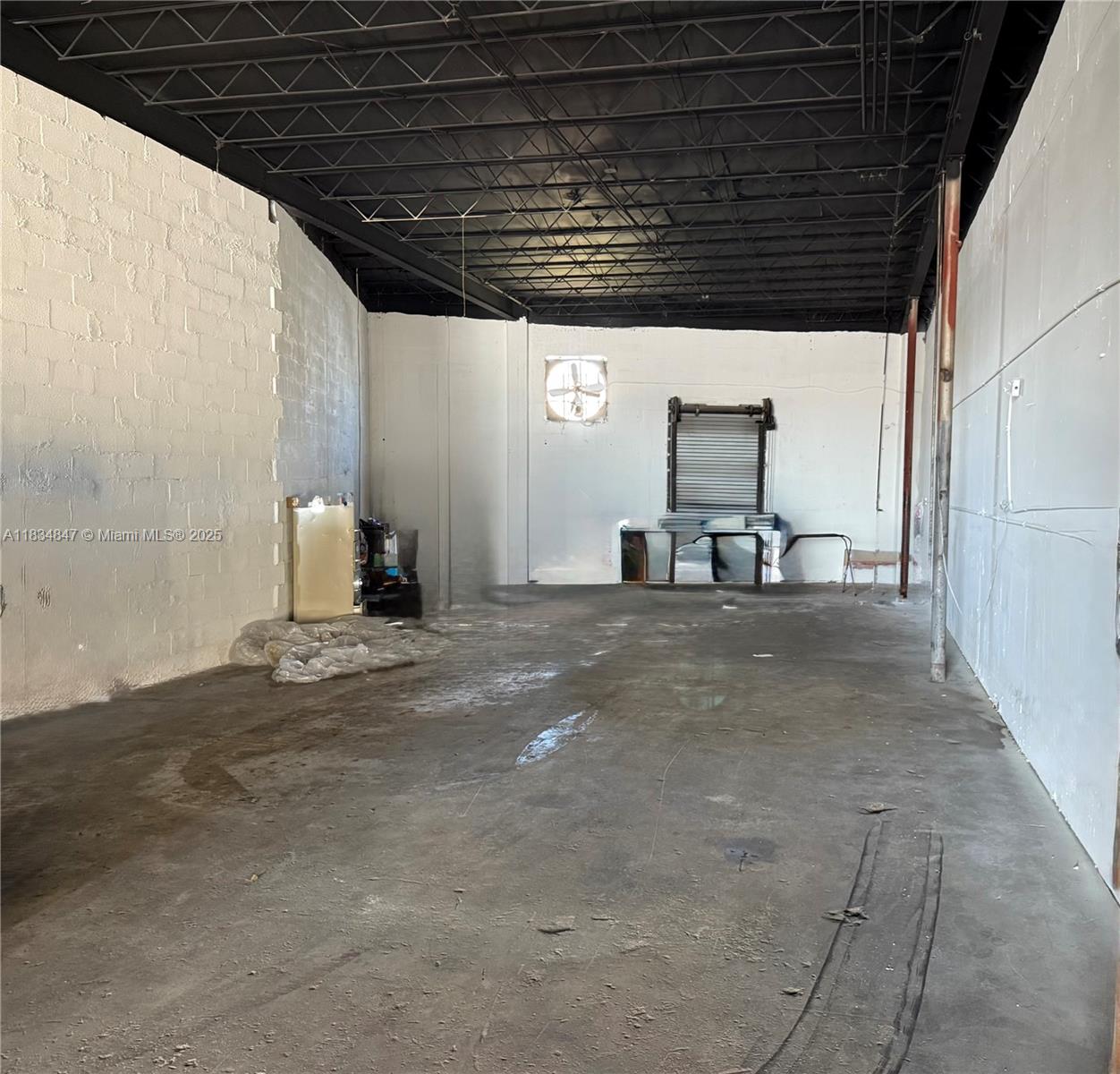 An empty industrial warehouse space features white concrete walls, a black ceiling, and a roll-up door — 3771 NW 51st St # B, Hialeah FL 33142, HIALEAH, FL
