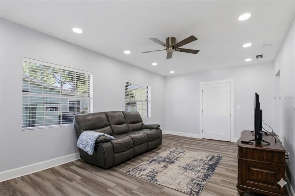 A living room features light gray walls, wood-look flooring, a gray sofa, and a ceiling fan — 4509 26TH AVENUE S, TAMPA, FL