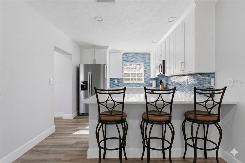 A kitchen features white cabinetry, a blue glass tile backsplash, and three bar stools — 4509 26TH AVENUE S, TAMPA, FL