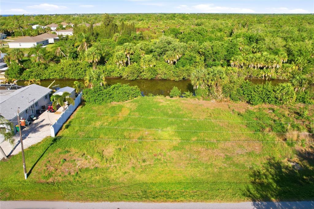 An aerial view shows a vacant grassy lot adjacent to a house and a canal — 3383 DESOTO DRIVE, PUNTA GORDA, FL