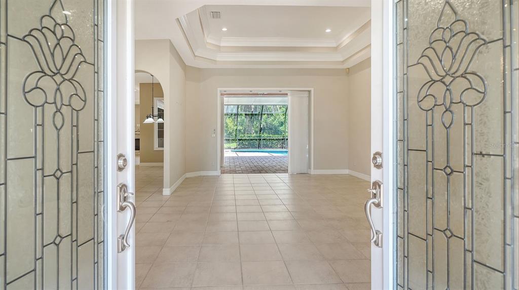 A view through a decorative glass front door into a tiled foyer with tray ceilings — 4769 SWEETMEADOW CIRCLE, SARASOTA, FL
